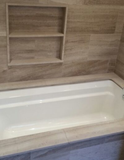 A modern bathroom featuring a built-in bathtub with beige tile surround and wall-mounted faucets.