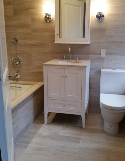 Modern bathroom interior with a beige color scheme, featuring a vanity, wall-mounted mirror, sconces, a bathtub, and a toilet.