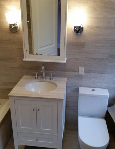 A modern bathroom with beige tiled walls featuring a white vanity, mirror, and toilet.