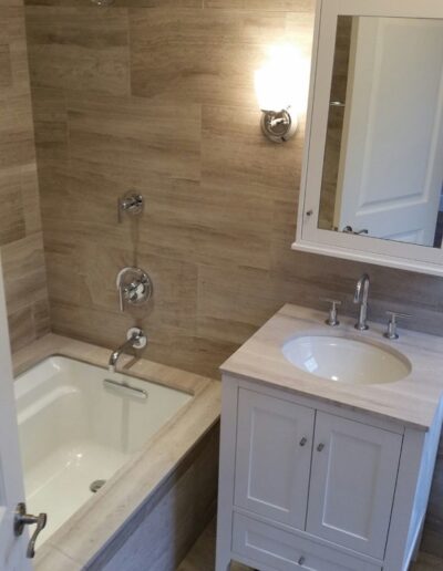 Modern bathroom interior with a bathtub, wall-mounted fixtures, vanity with sink, and a mirror.