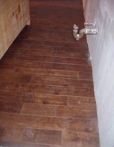 Wooden flooring with a water meter and pipes along a wall.