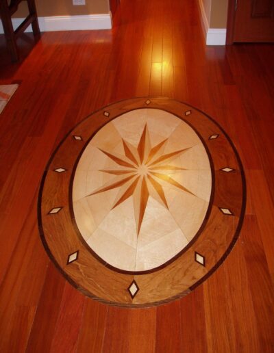 Inlaid wooden floor medallion with star pattern in a polished hardwood hallway.