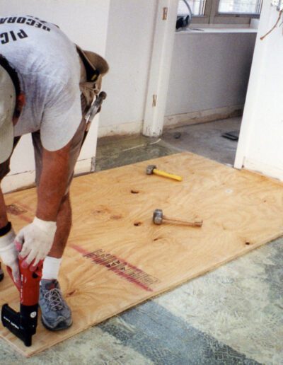 A person installing plywood flooring with tools.