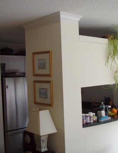 An interior view of a kitchen and dining area with a decorative mirror, framed pictures, and a hanging plant.