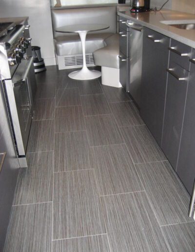 Modern kitchen with stainless steel appliances and gray cabinetry on a textured tile floor.