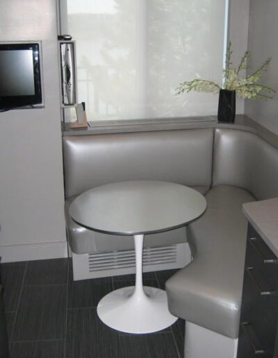 A modern kitchen nook with built-in seating, a small white table, and stainless steel appliances.