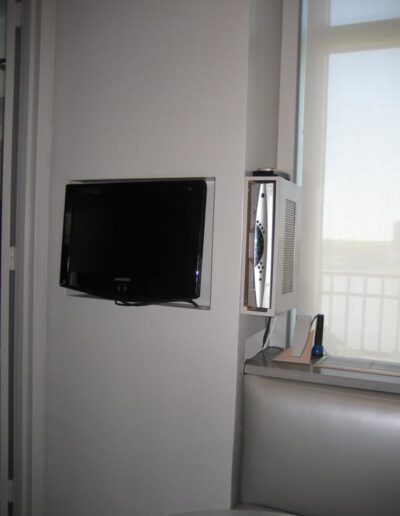 Flat-screen tv mounted on a wall next to a window with closed blinds.