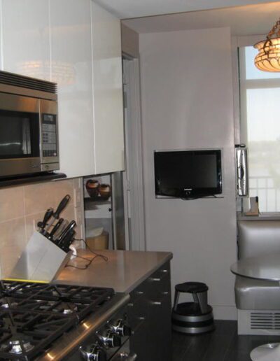 A modern kitchen with stainless steel appliances and a small tv mounted on the wall.