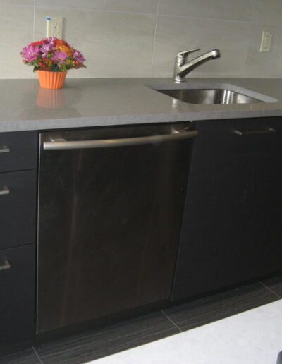 Modern kitchen countertop with stainless steel sink and black cabinets, adorned with a bouquet of flowers in an orange vase.