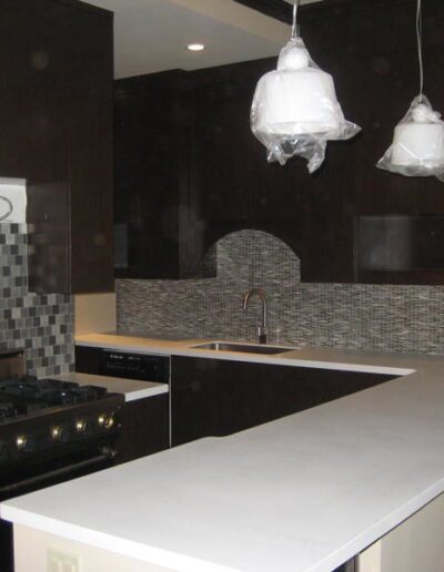 Modern kitchen interior with dark cabinets, stainless steel appliances, mosaic backsplash, and white countertop.