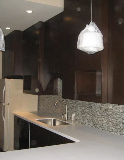 A modern kitchen with dark wood cabinetry, stainless steel appliances, mosaic backsplash, and pendant lights covered in protective wrapping.