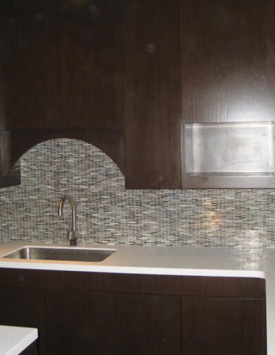 Modern kitchen with dark wood cabinets, mosaic backsplash, and stainless steel sink.