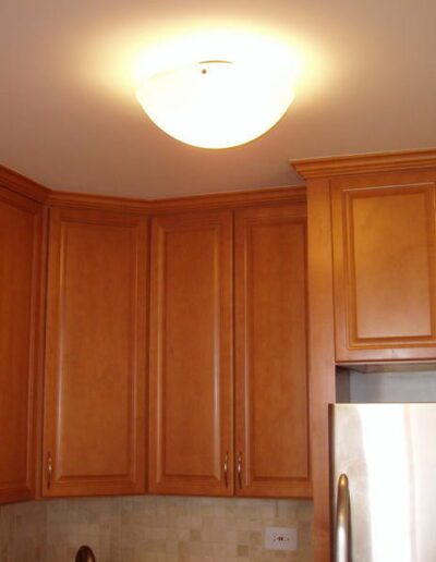 Kitchen interior with wooden cabinets, a stainless steel refrigerator, and a ceiling-mounted light fixture.