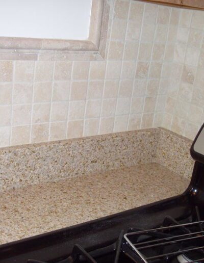 Beige tiled kitchen backsplash above a speckled countertop with a black stove to the right.