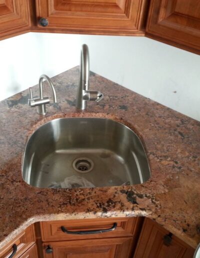 Stainless steel kitchen sink with a modern faucet, set in a granite countertop and wooden cabinets.