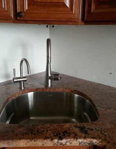 A stainless steel undermount sink with a modern faucet, set in a granite countertop, beneath wooden cabinets.