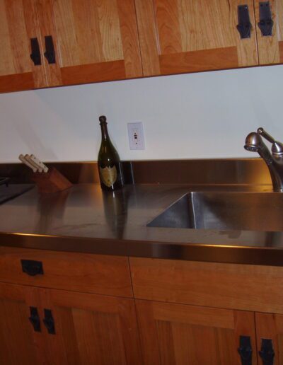 A kitchen countertop with a stainless steel sink, wooden cabinets, and a lone bottle to the left.