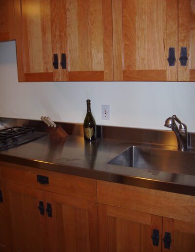 A kitchen corner with wooden cabinets and a stainless steel sink, featuring a lone green bottle on the countertop.