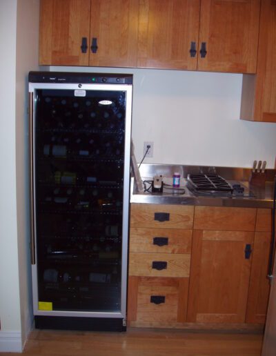 A wine cooler full of bottles integrated into a modern wooden kitchen beside a sink and gas stove.