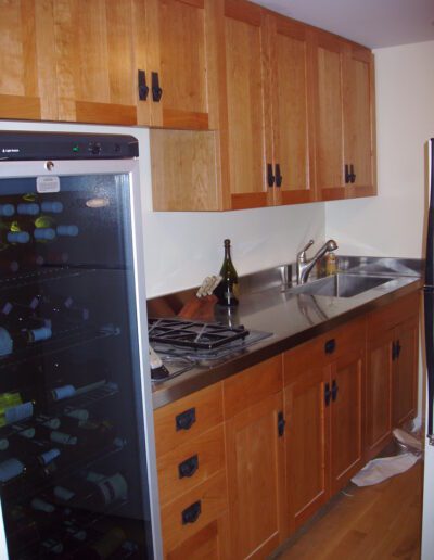 A compact kitchen with wooden cabinets, stainless steel countertop and sink, a gas stove, and a wine cooler.