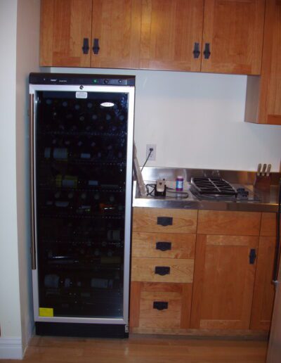 A wine refrigerator stocked with bottles is placed in a modern kitchen setting.