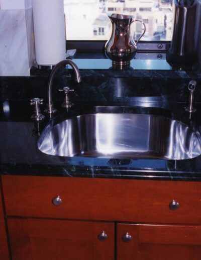 Modern kitchen with stainless steel sink, granite countertops, and red wooden cabinets.