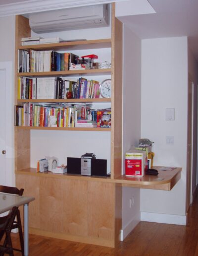 A well-organized home office space with a wall-mounted bookshelf, an air conditioning unit above, and a floating desk with office supplies.