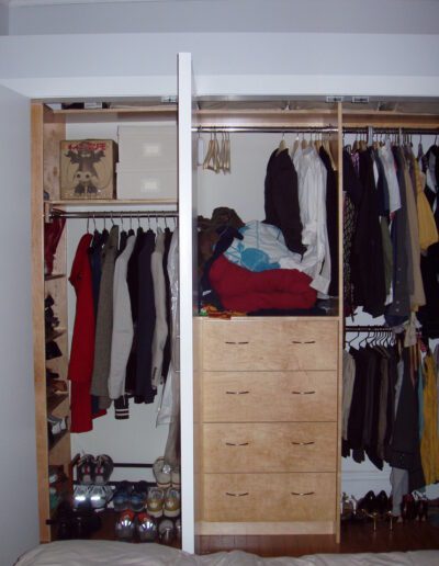 An open wardrobe filled with various clothes and shoes, with a stack of clothes on a shelf and closed drawers in the center.