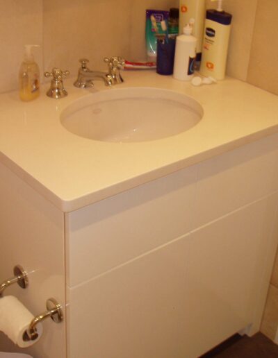 A white bathroom vanity with a sink, faucet, and various toiletry items on the countertop.