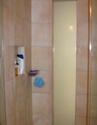 A shower corner with beige tiles and a blue loofah hanging on the wall.