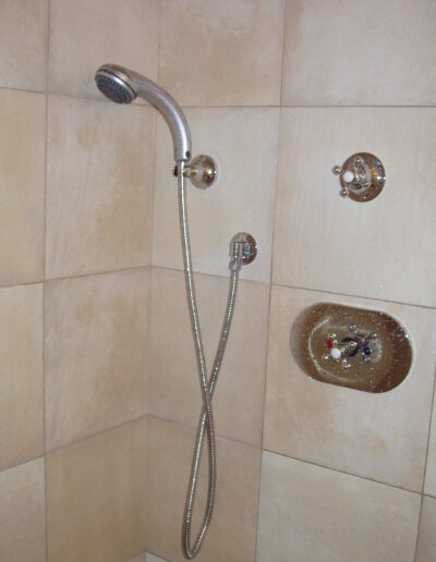 A shower with beige tiles, featuring a mounted shower head and faucet controls.