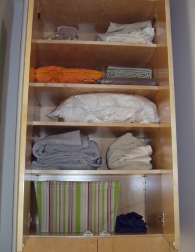 An organized wooden wardrobe with neatly folded linens and clothing items on shelves.