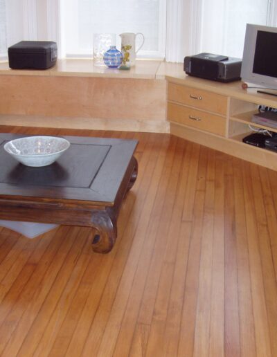 A living room with wooden flooring featuring a coffee table, a couch, and a television on a stand.