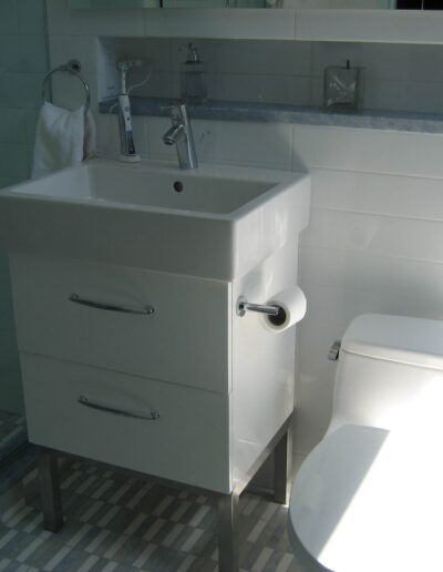 A modern bathroom with a white sink cabinet, toilet, and a shower in the background.