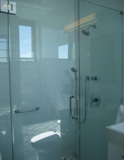 Glass-enclosed walk-in shower with white tiles and modern fixtures in a well-lit bathroom.