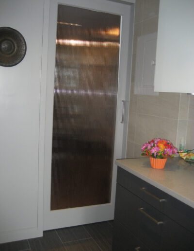 A modern bathroom with a ribbed glass door, dark cabinets, and a bouquet of flowers on the countertop.