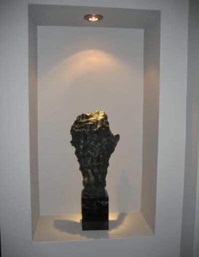 Bronze sculpture of a hand presented in a white niche with spotlighting.