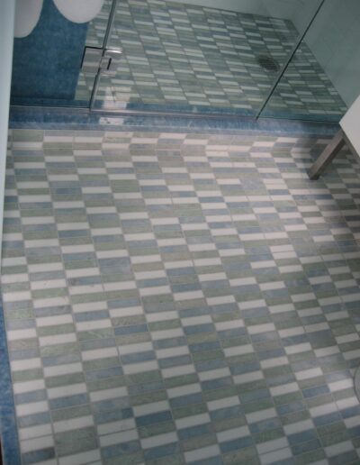 A bathroom with blue and white tiled flooring extending into a glass-enclosed shower area.