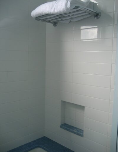 A white tiled bathroom corner with a small built-in shelf and a towel rack above it.