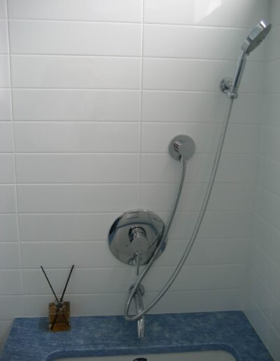 A modern bathroom shower with white tiles, a handheld showerhead, and a blue countertop.