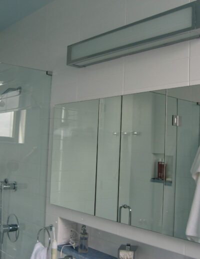 A modern bathroom with a glass shower enclosure, white tiles, and a large mirror over the sink.