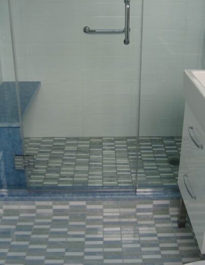 A modern bathroom with blue and white tiles, featuring a walk-in shower and a white pedestal sink.