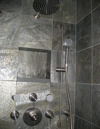 A modern shower with a rainfall showerhead and multiple body jets against a gray slate tile background.