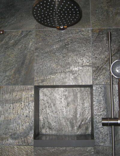 A modern shower with a rain shower head and a handheld shower wand, featuring dark stone tiles.