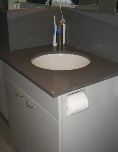 Modern bathroom interior featuring a grey vanity with a white basin, silver faucet, and a towel hanging on the side.