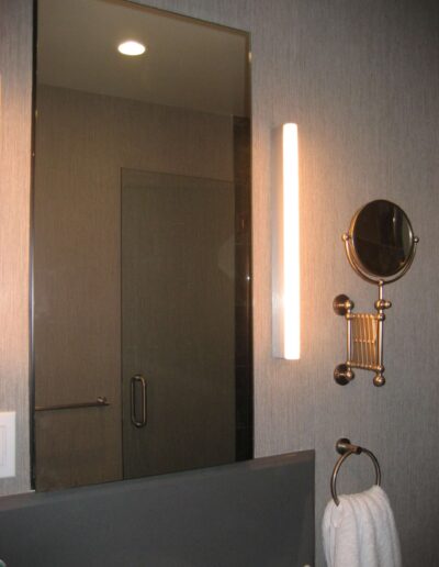 Modern bathroom interior with a glass shower door, a vertical light fixture, and a magnifying vanity mirror.