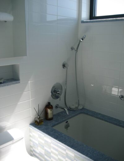 A modern, white-tiled bathroom with a bathtub and a wall-mounted shower fixture.