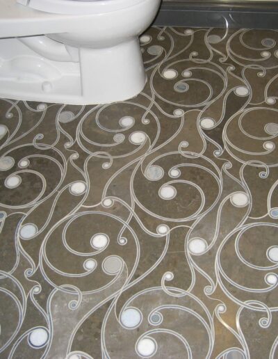 A bathroom interior focusing on patterned tile flooring with a toilet in the upper left corner.