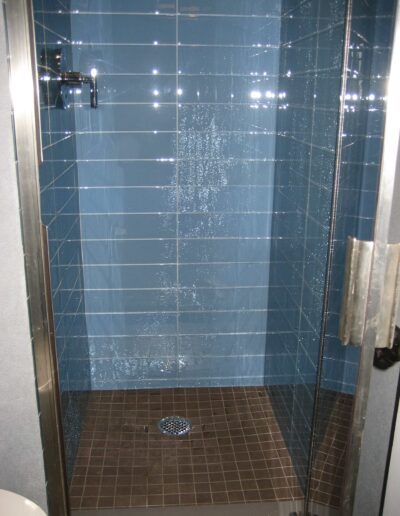 A modern shower cubicle with blue tiles and a glass door, showing water droplets on the glass indicating recent use.