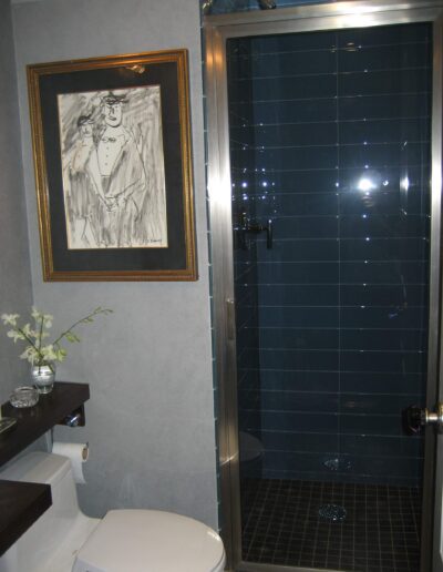 A modern bathroom with a glass shower enclosure, white toilet, and a framed picture hanging on the wall.